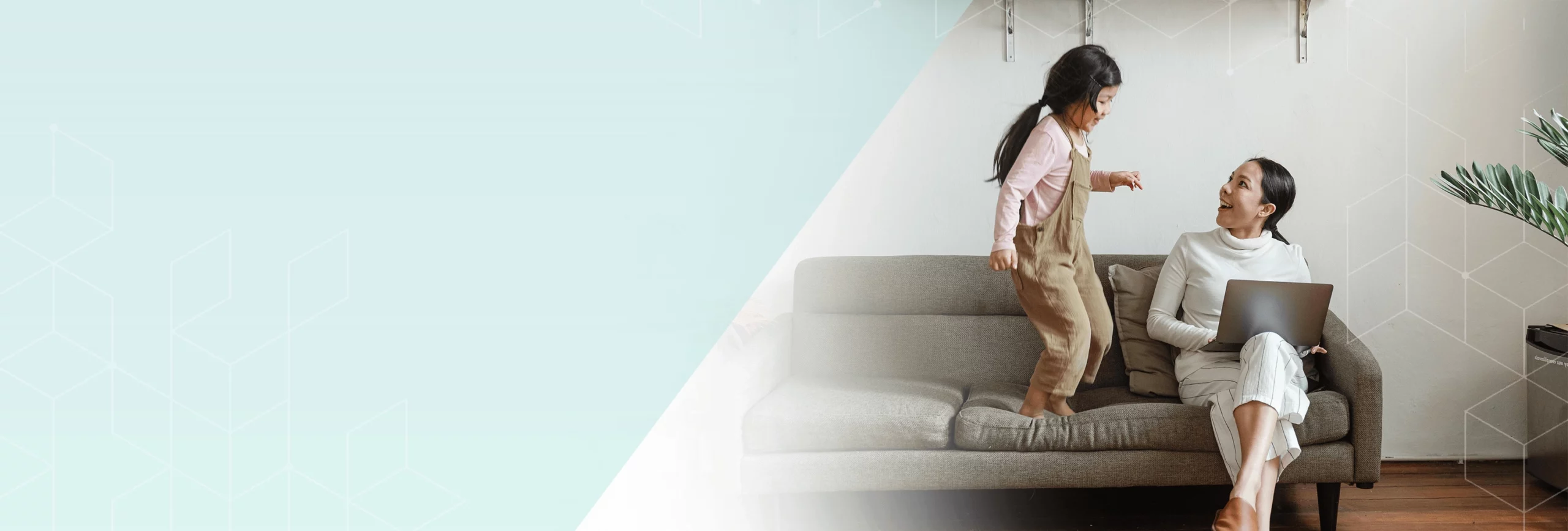 daughter jumping on couch while mother is doing work on laptop