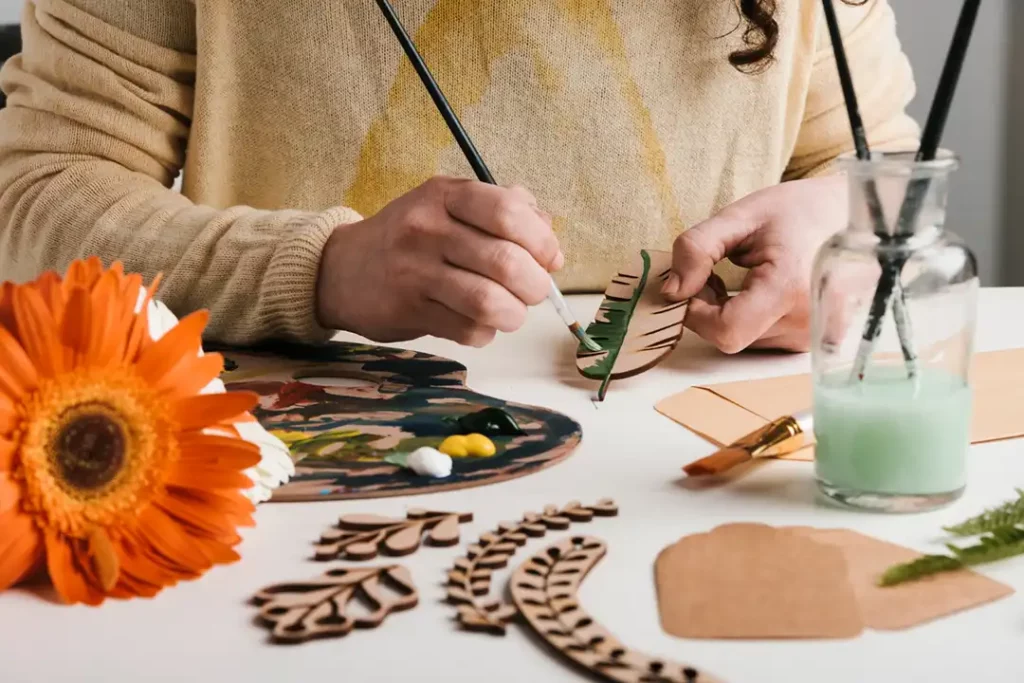 Close up image of woman in yellow sweater painting wooden flowers